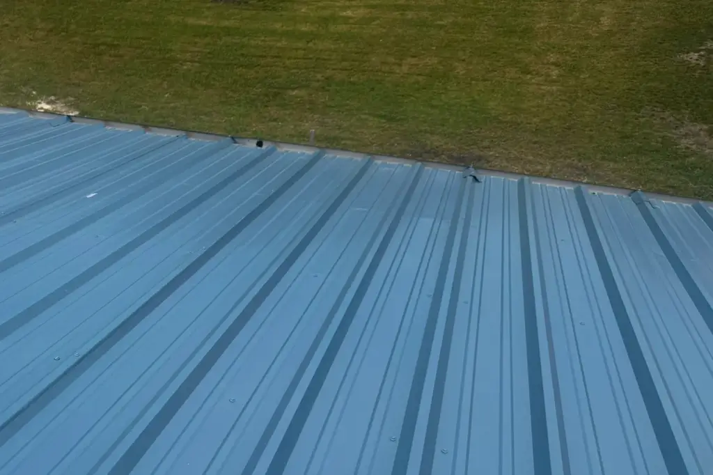Blue standing-seam metal roof panels meeting a lawn