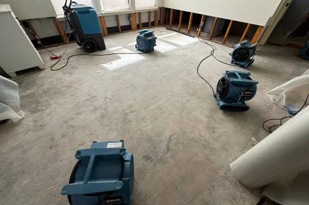 Dehumidifier and air movers drying a room after water damage