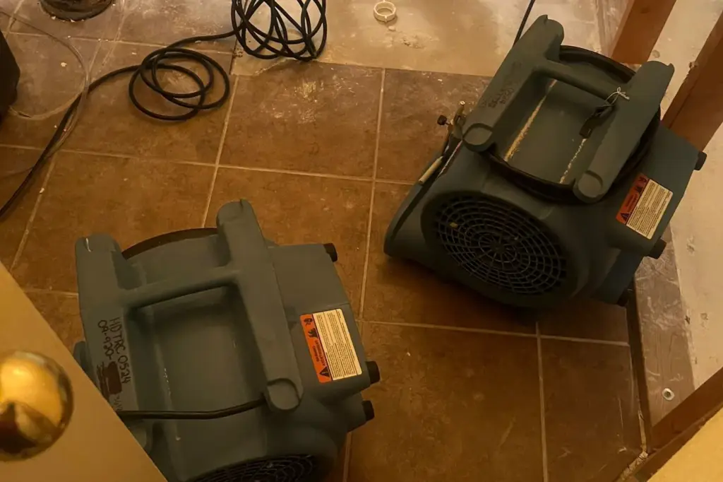 Two air movers drying a tiled bathroom with open wall cavities